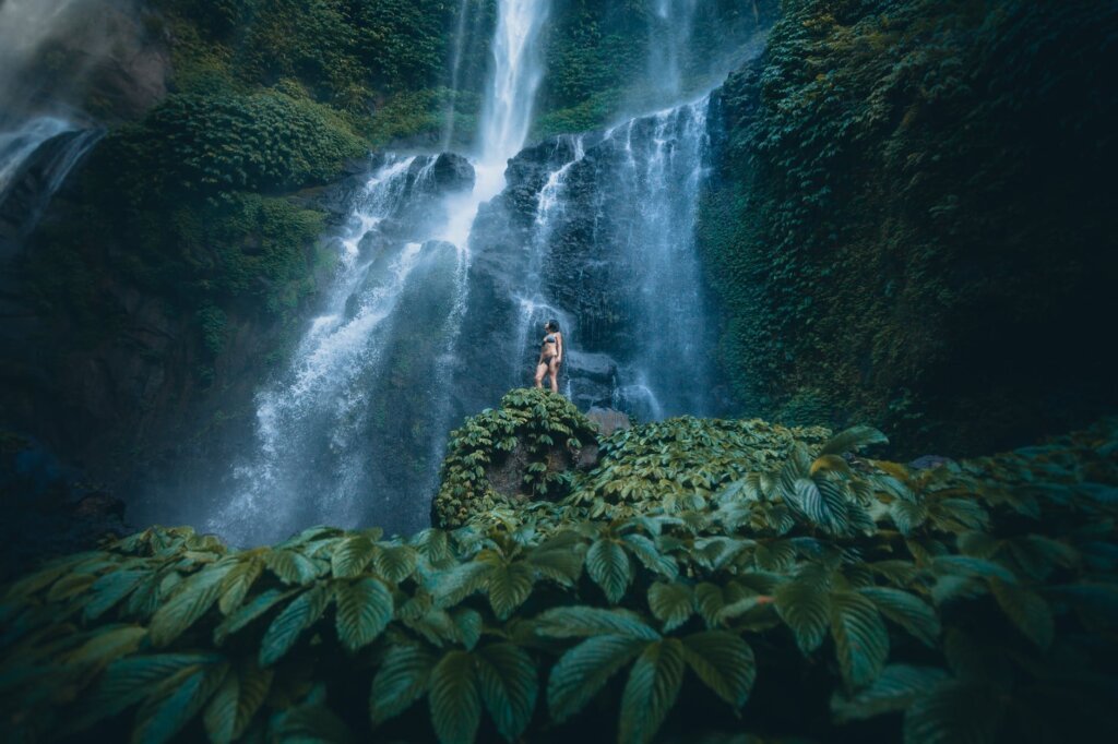 a picturesque view of a woman standing near a waterfall